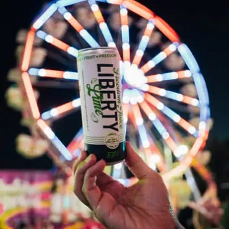 A can of Liberty Lime held up in front of a lit ferris wheel
